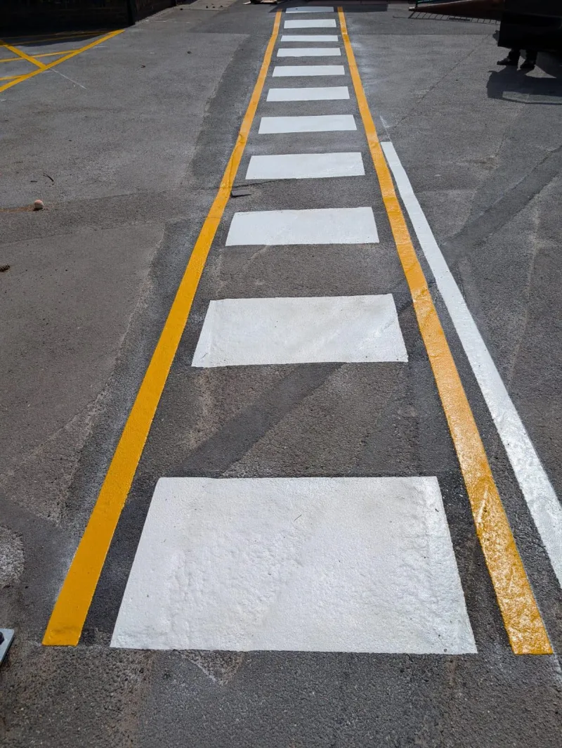 White pedestrian crossing bars and double yellow lines marked across a site access road