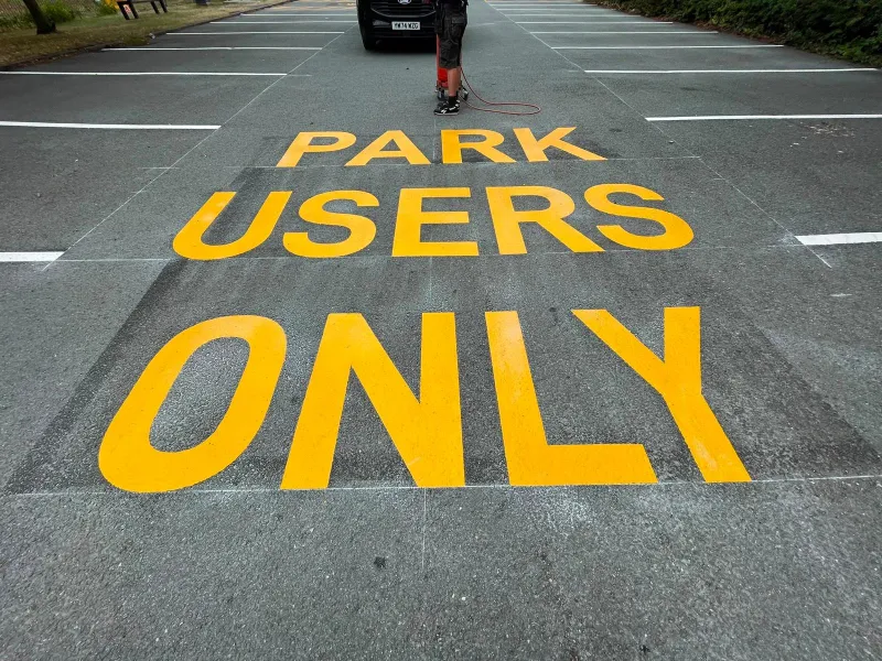 Bold yellow PARK USERS ONLY lettering marked across a tarmac access road