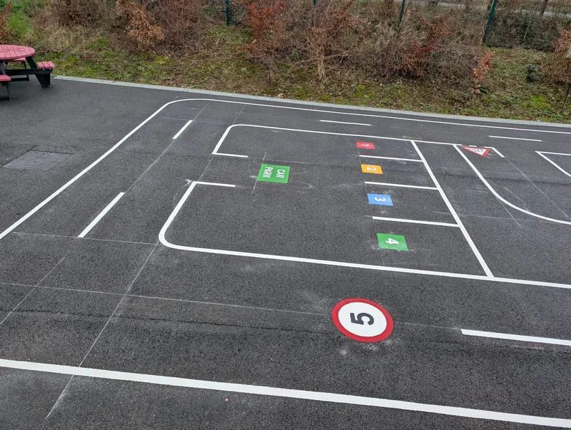 White roadway and directional markings, numbered bays and a speed roundel laid on dark asphalt