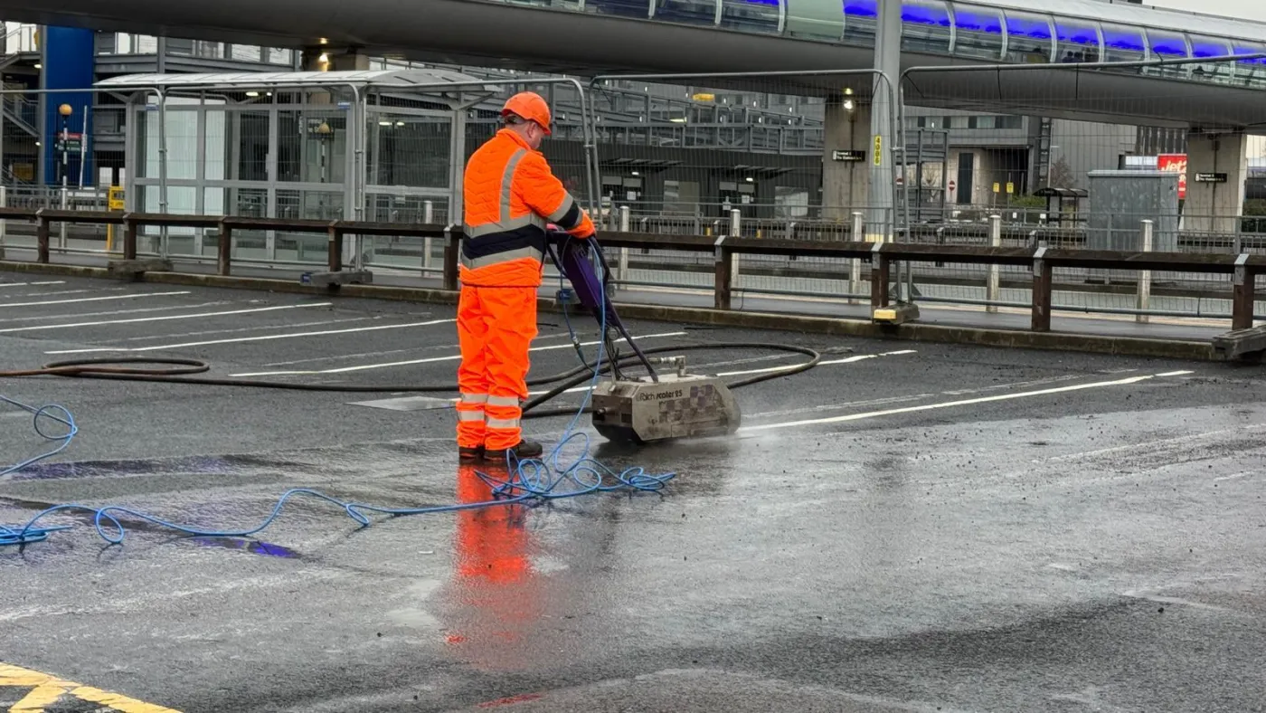 A Uniplay operative in orange hi-vis blasting a line marking off tarmac with an ultra high pressure water lance