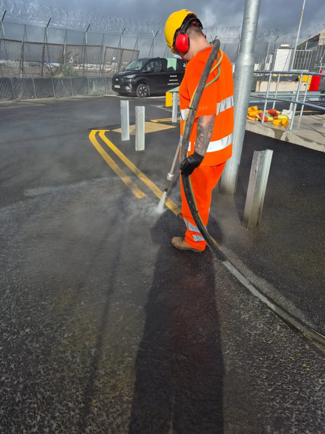 A Uniplay operative using the UHP water lance to blast yellow line markings off tarmac, spray and steam rising
