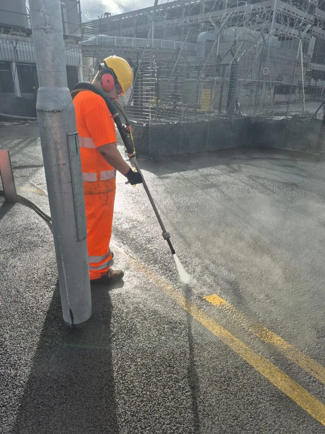 Controlled water-based blasting removing surface markings beside a steel post on an industrial site, spray and steam rising